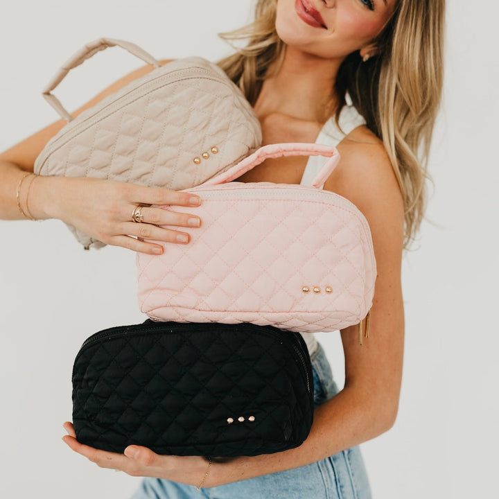 Woman holding three quilted handbags in beige, pink, and black.
