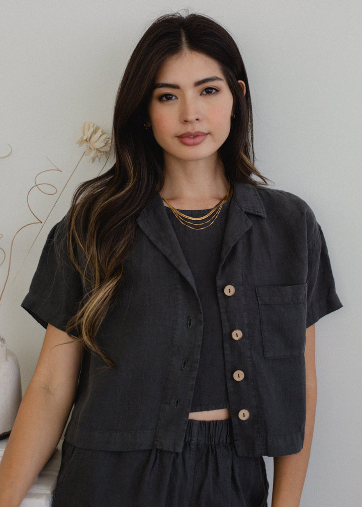 Woman wearing a dark gray button-up shirt over a black top with a white background