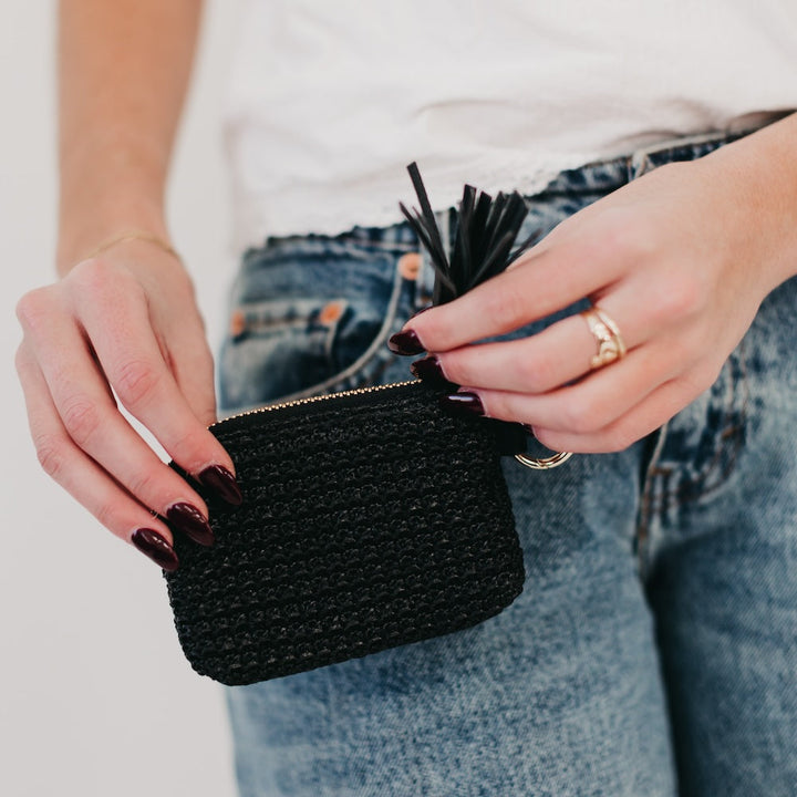 Person holding a black woven pouch with a blurred background