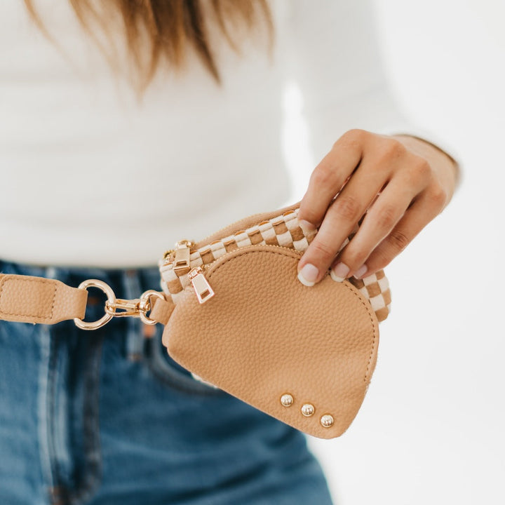 Beige pouch and checkered pouch with a strap held by a person wearing a white shirt and blue jeans.