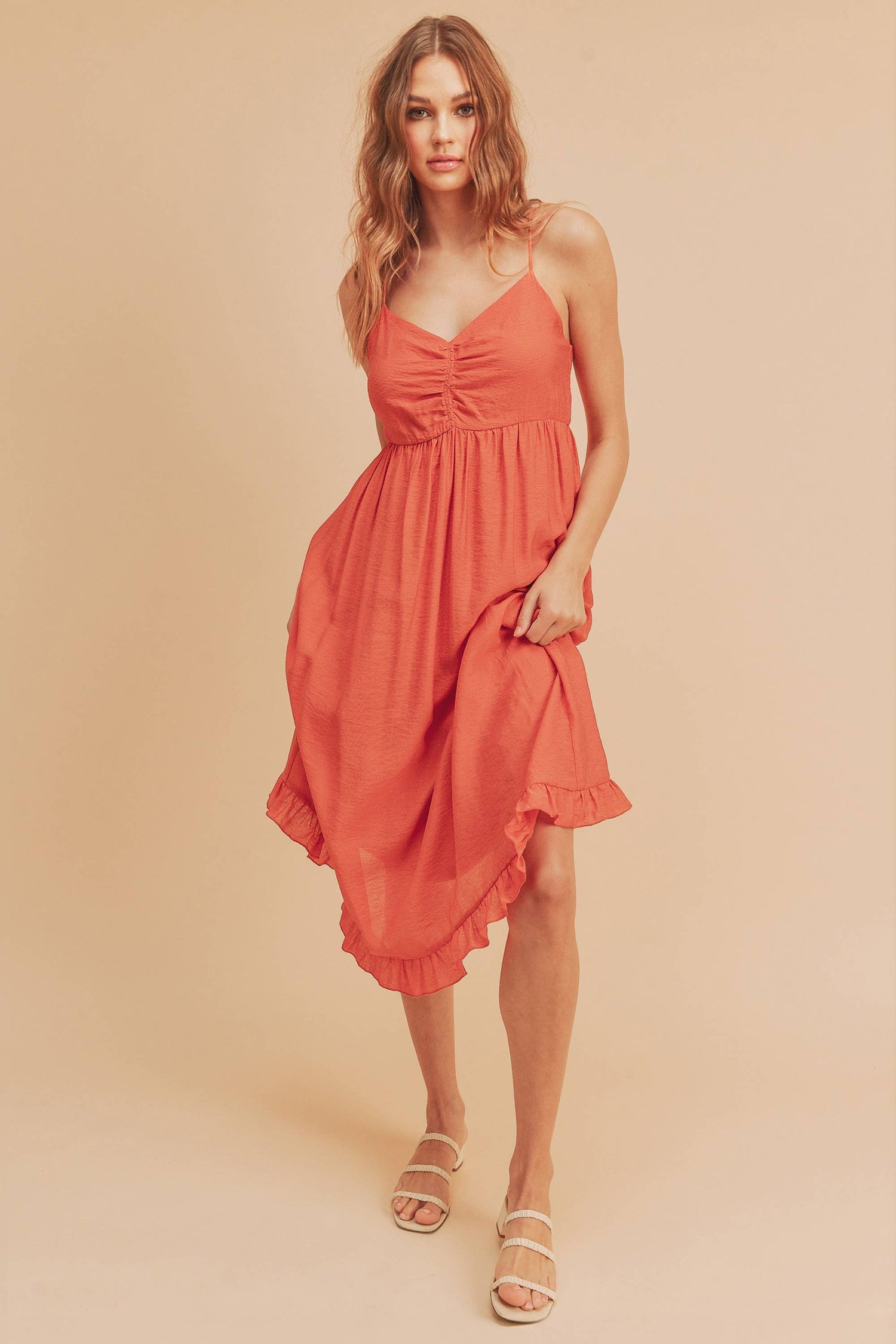 A model wearing a coral maxi dress with adjustable spaghetti straps, a lined bodice, and a ruffled hem.