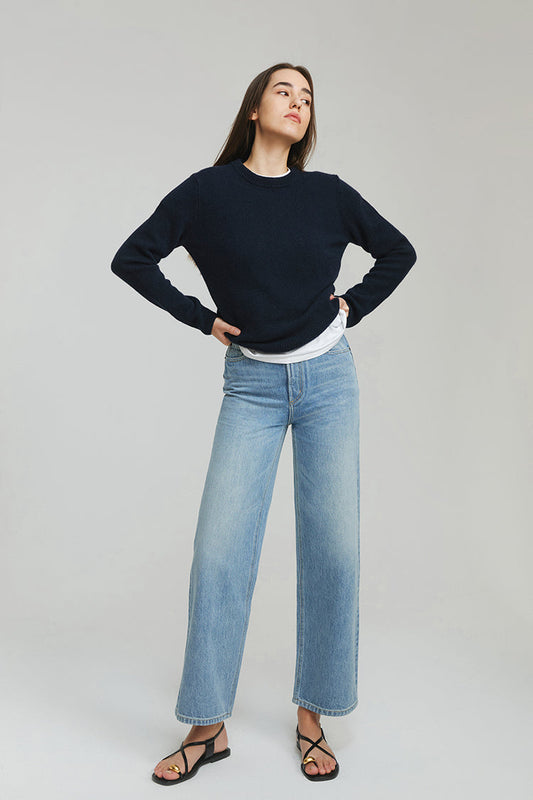 Person wearing a navy sweater and light blue jeans on a plain background