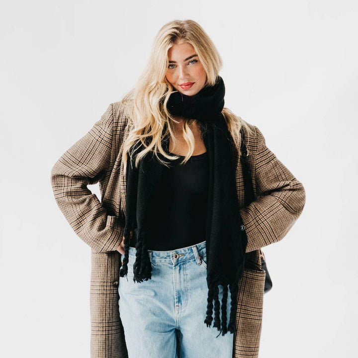 Woman wearing a plaid coat, black scarf, black top, and light blue jeans on a white background