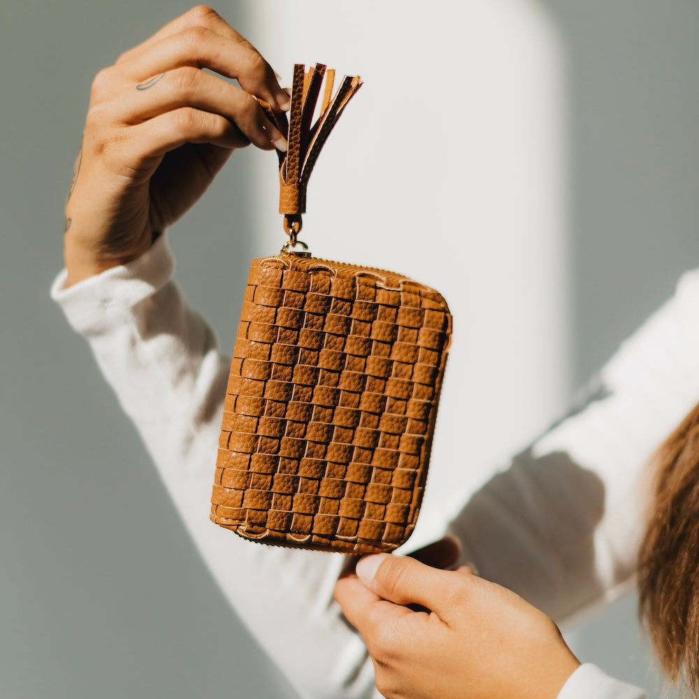 Brown woven purse held by a person with a blurred background