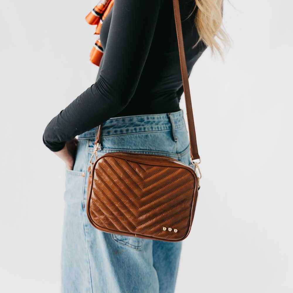 Person wearing a brown quilted crossbody bag with a plain background