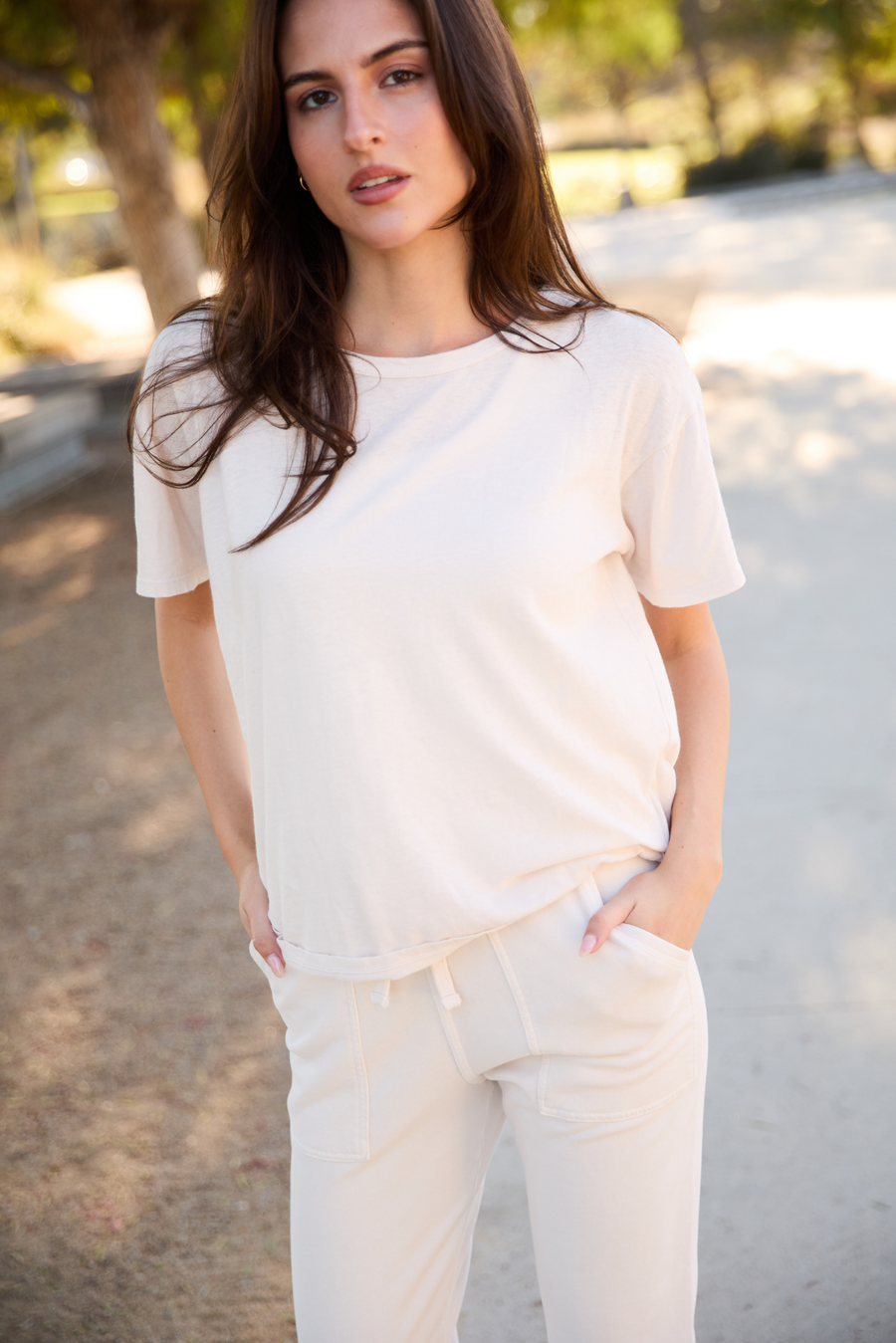 Woman wearing a white outfit standing outdoors with trees in the background