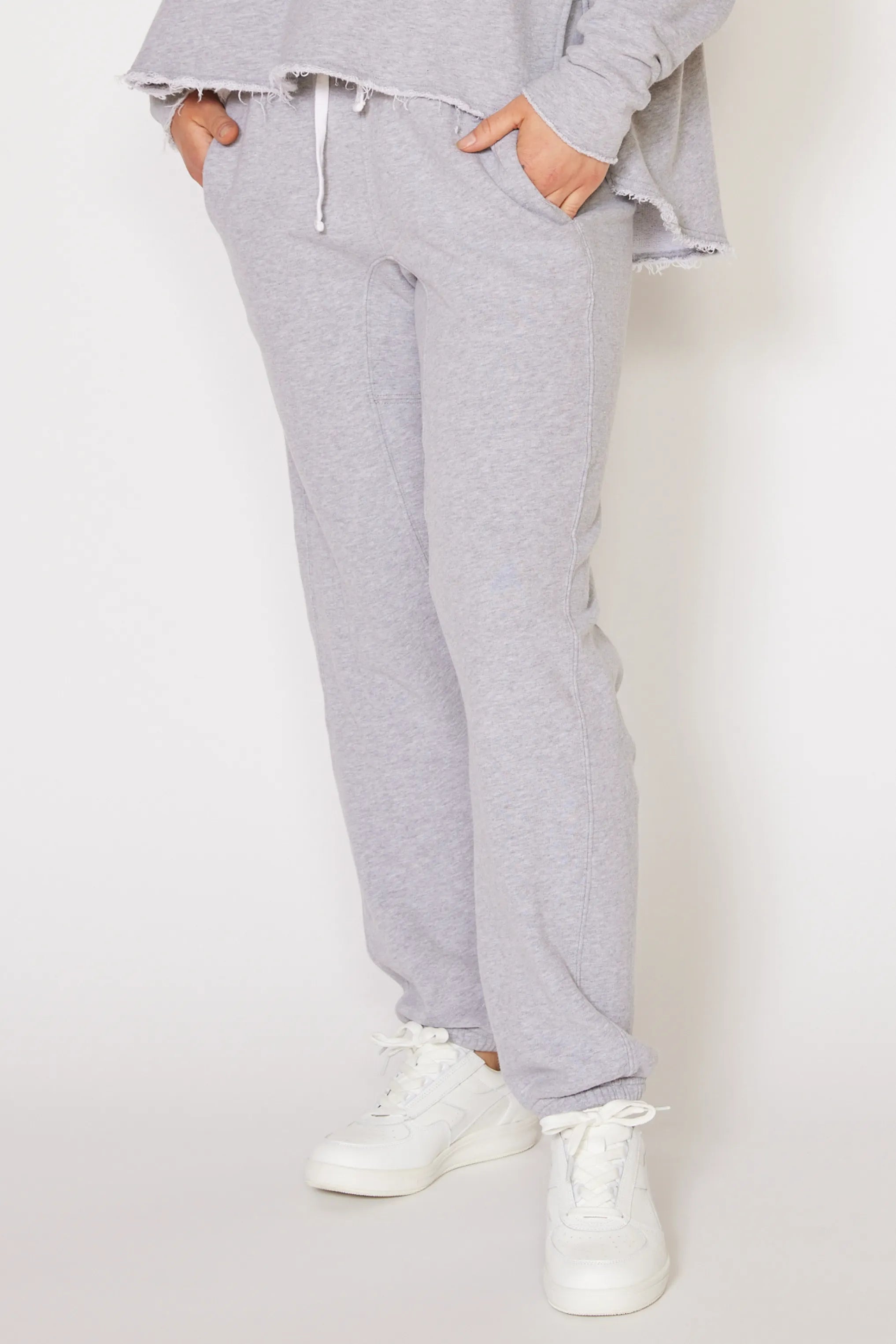 Person wearing gray sweatpants and white sneakers on a plain background
