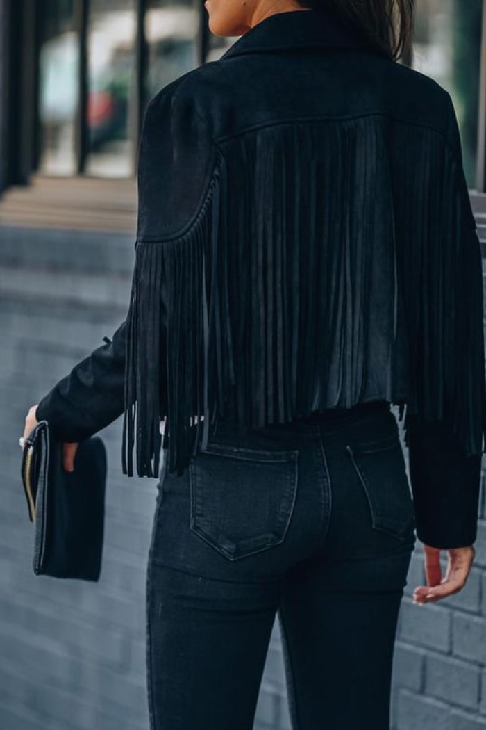 Person wearing a black fringed vegan suede jacket and dark jeans against a blurred background