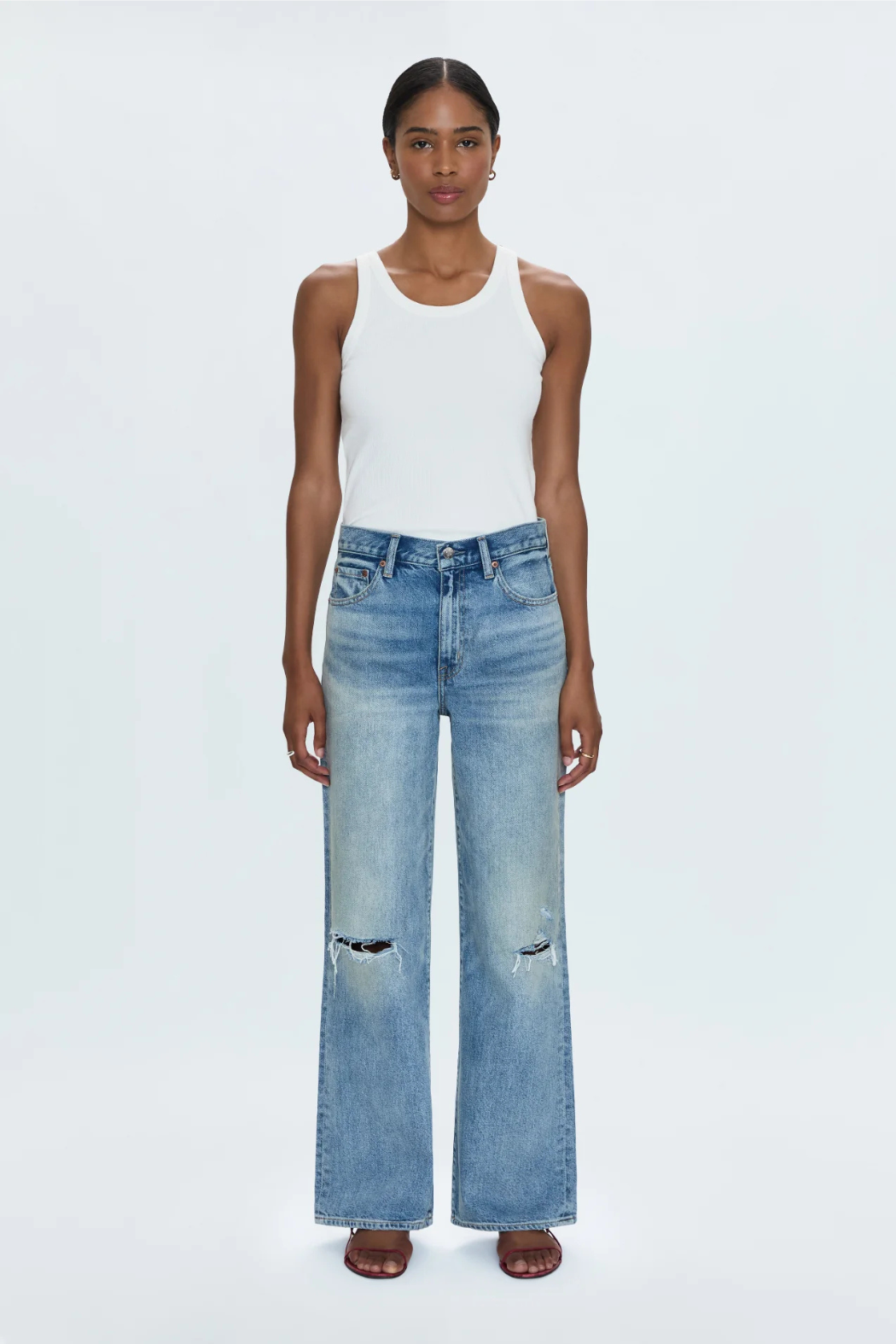 Woman wearing a white tank top and blue jeans on a white background