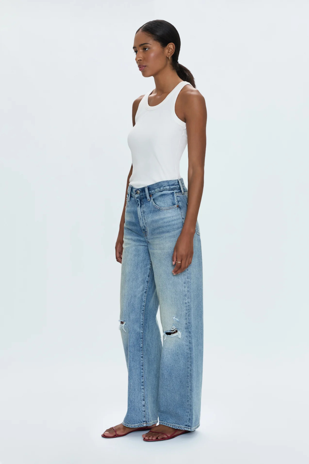 Woman wearing a white tank top and light blue jeans on a white background