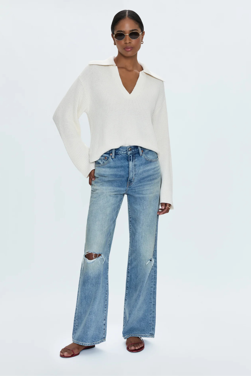 Woman wearing a white sweater and blue jeans on a white background
