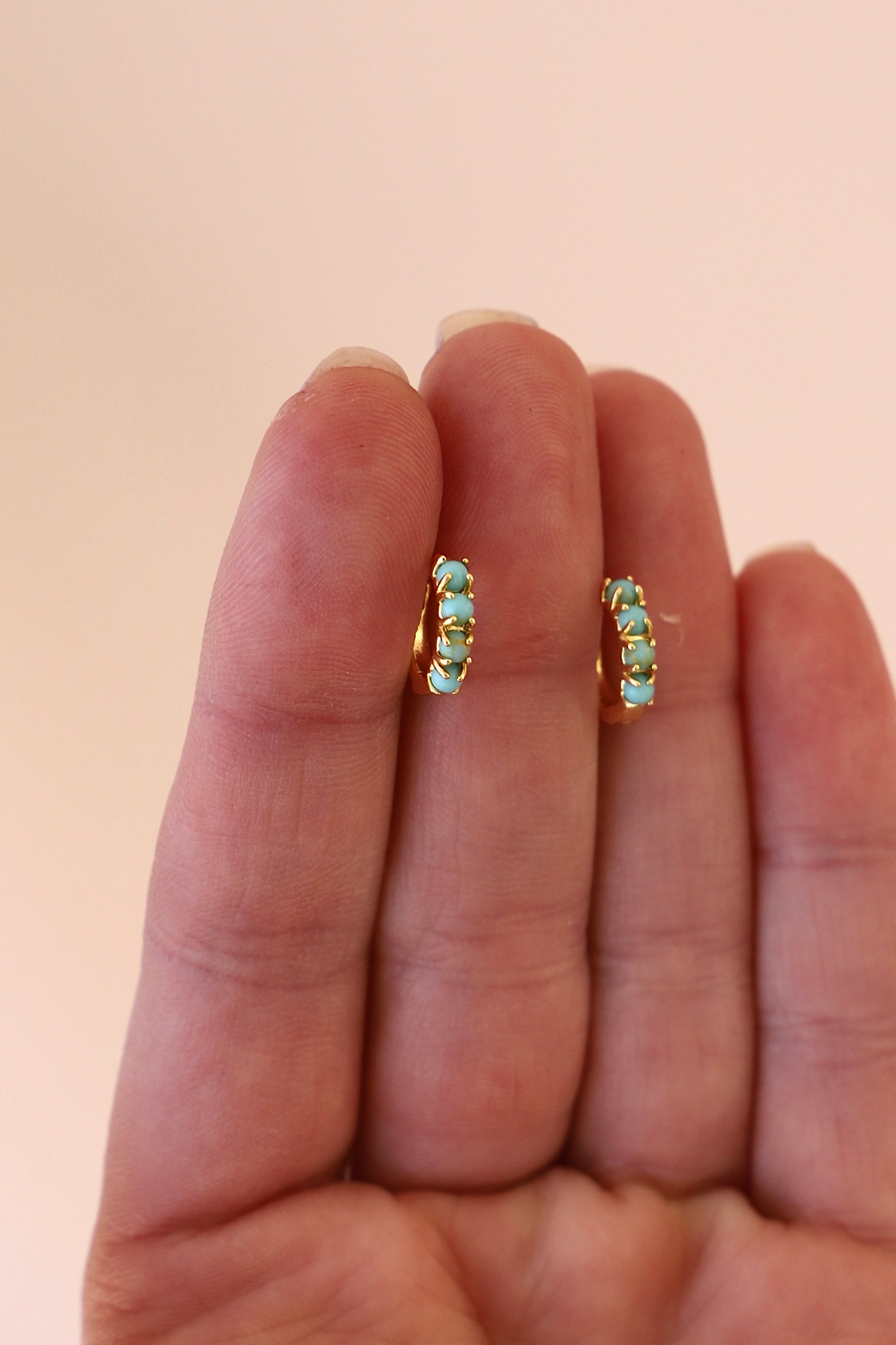 Pair of emerald green earrings held between two fingers against a beige background