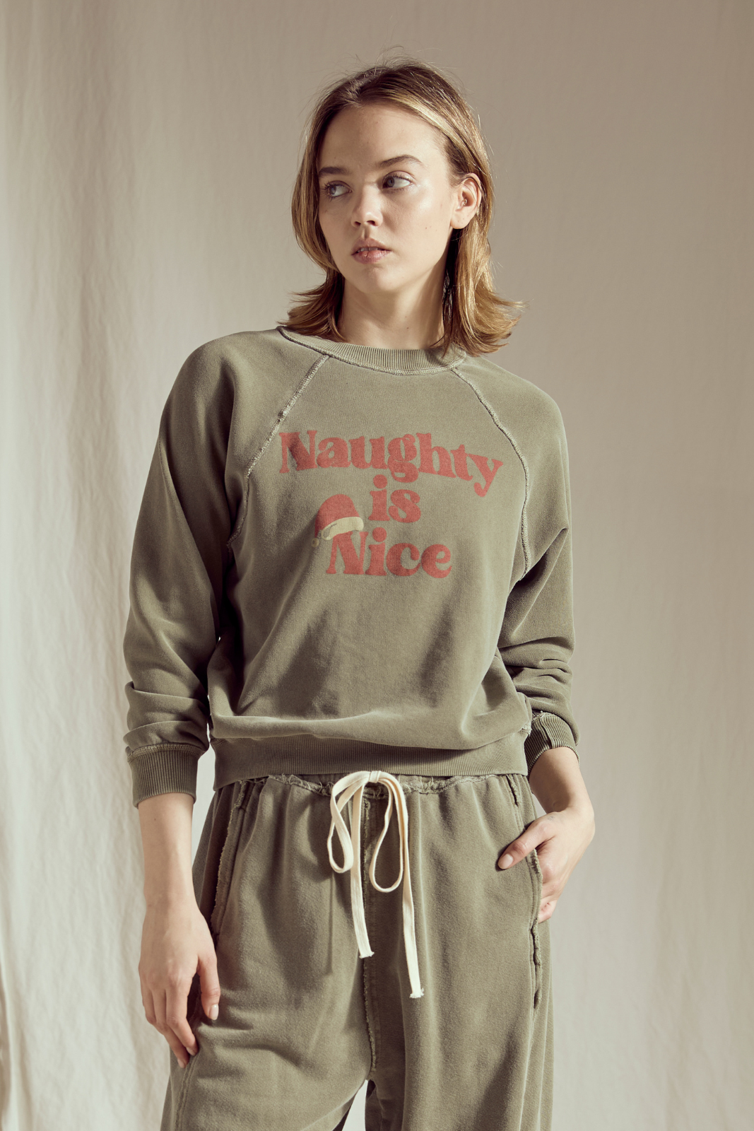 Woman wearing a green sweatshirt with 'Naughty is Nice' text and matching pants against a neutral background