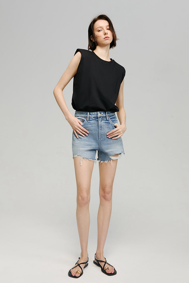 Woman wearing a black sleeveless top and denim shorts on a gray background