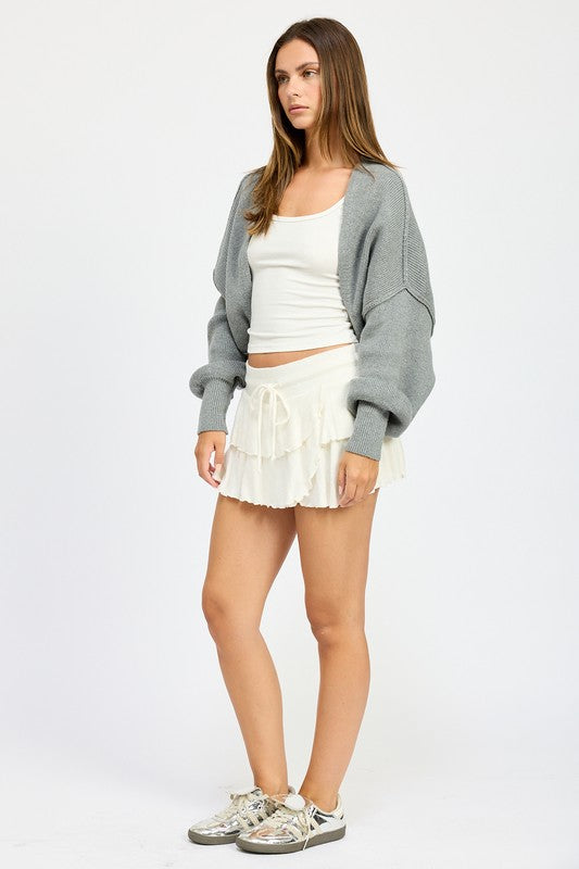 Person wearing white tank and skirt with oversized shrug cardigan in gray