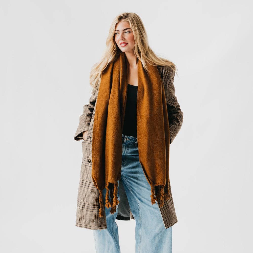 Woman wearing a brown scarf, plaid coat, and blue jeans on a white background
