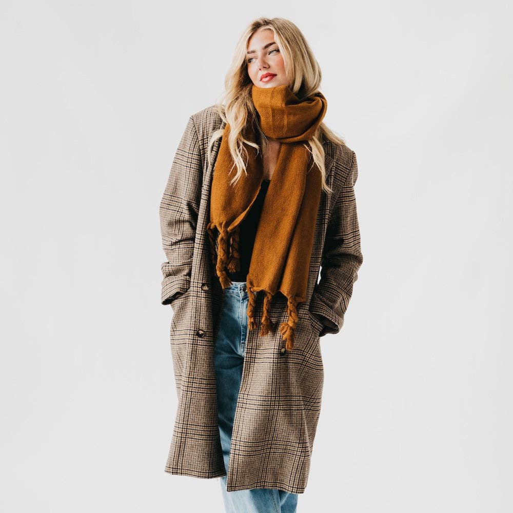 Woman wearing a plaid coat and caramel colored scarf against a white background