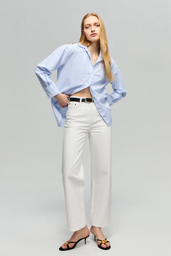 Woman wearing a light blue shirt and white pants on a gray background