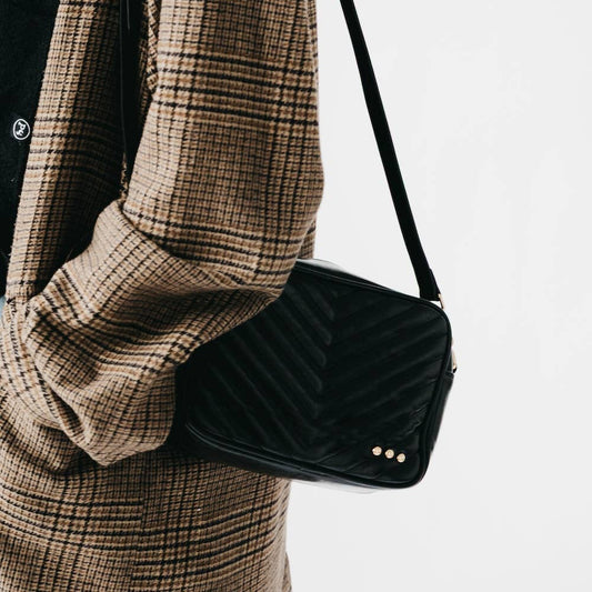 Person wearing a plaid coat holding a black velvet handbag on a light gray background