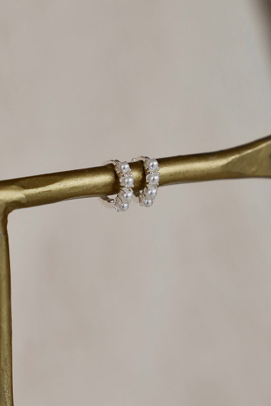 Pair of pearl hoop earrings on a gold branch with a neutral background
