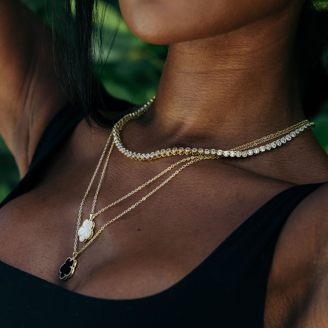 Close-up of a person wearing multiple gold necklaces with greenery in the background