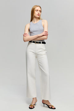 Woman wearing a gray tank top and white pants with a black belt on a light gray background
