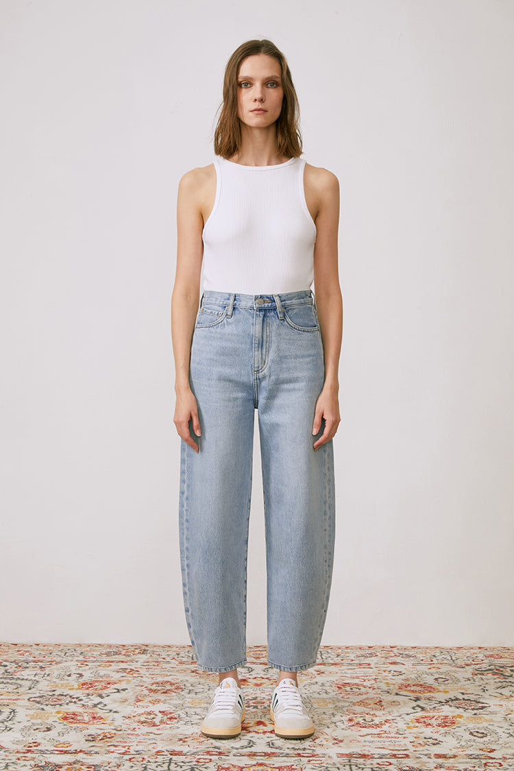 Woman wearing light blue jeans and a white tank top on a patterned rug.
