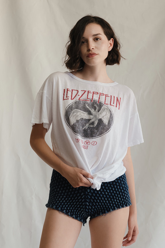 Woman wearing a white LED Zeppelin t-shirt with a graphic design on a plain background