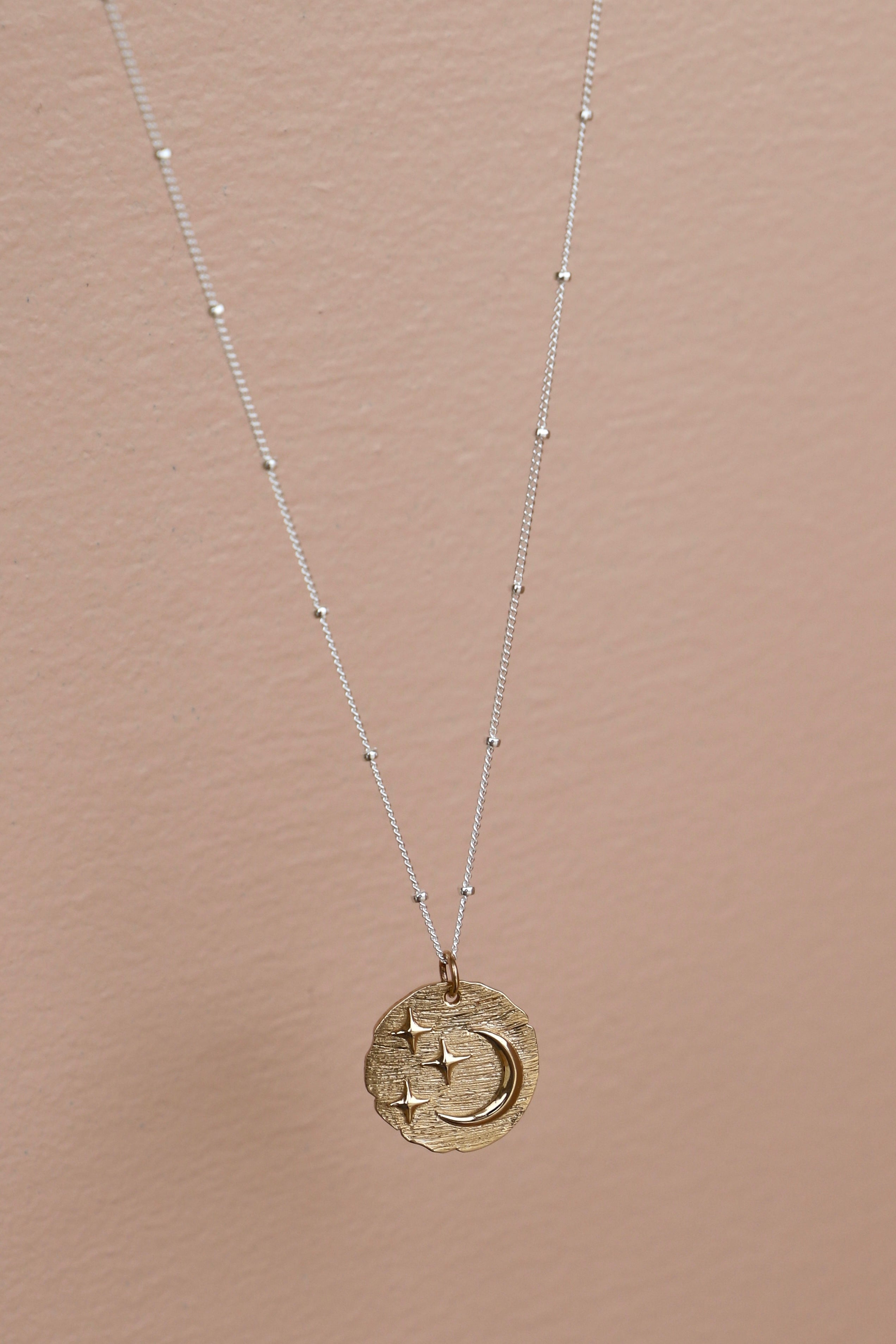 Gold necklace with a circular pendant on a beige background