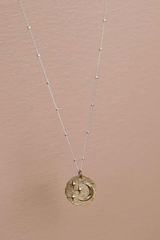 Gold necklace with a circular pendant on a beige background