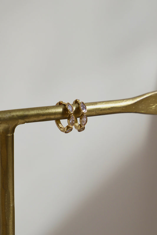 Gold ring with a central stone on a gold stand against a neutral background