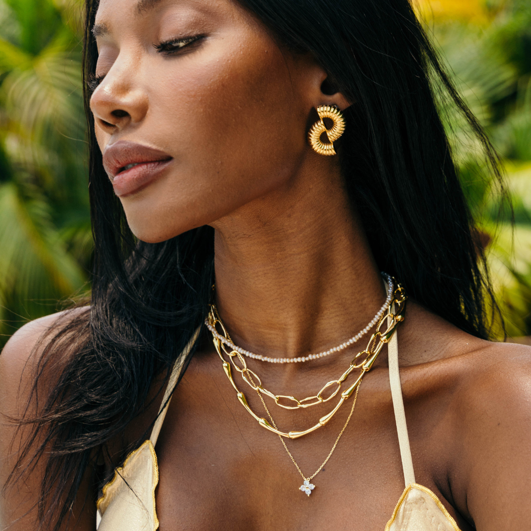 Woman wearing gold jewelry with a tropical background