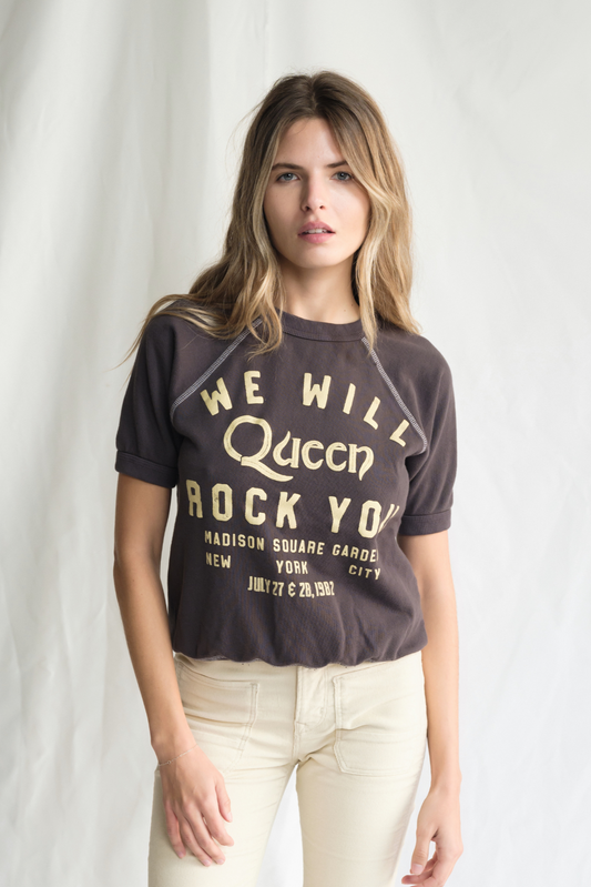 Woman wearing a t-shirt with 'We Will Queen Rock You' text on a plain background