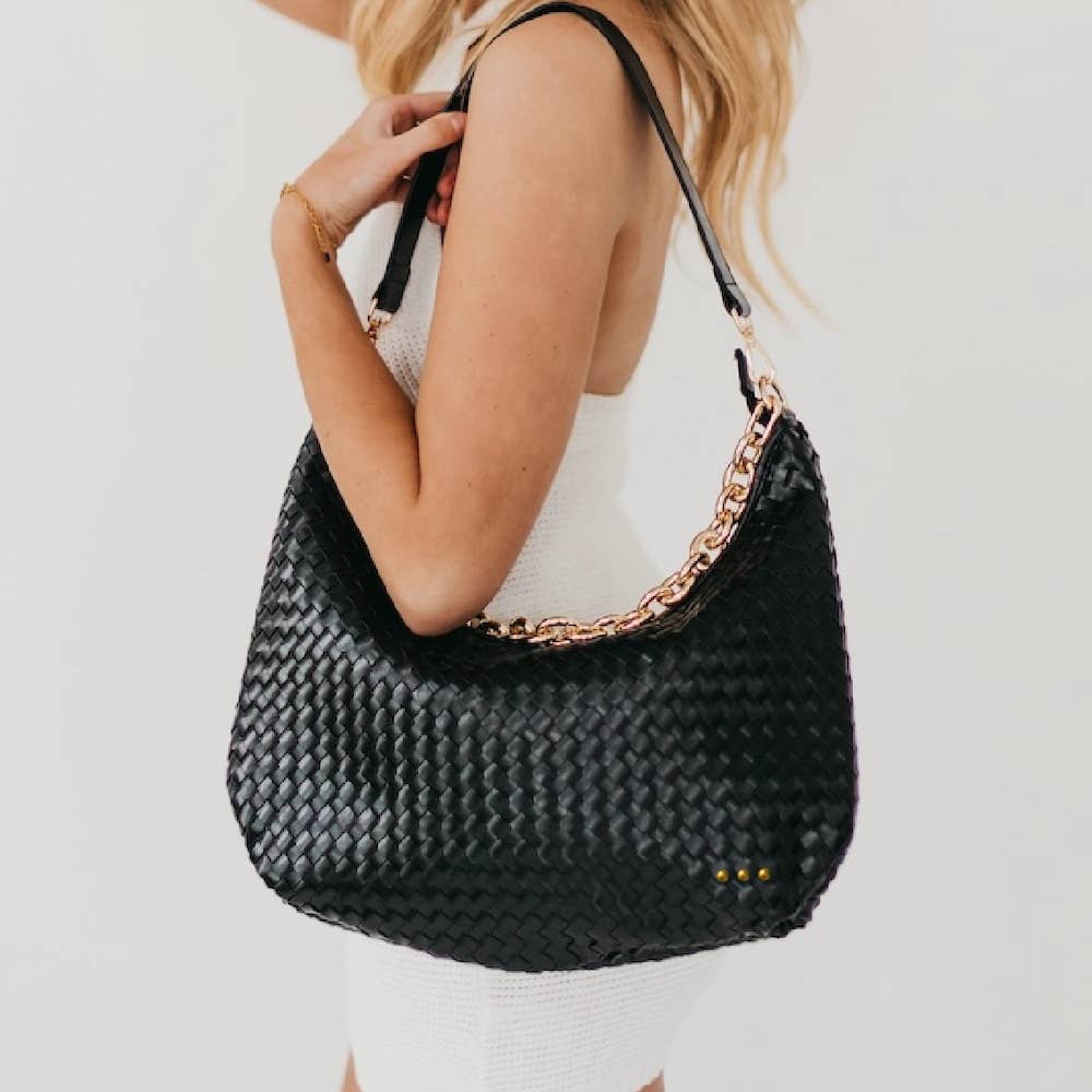 Black woven handbag with a chain detail held by a person against a light background