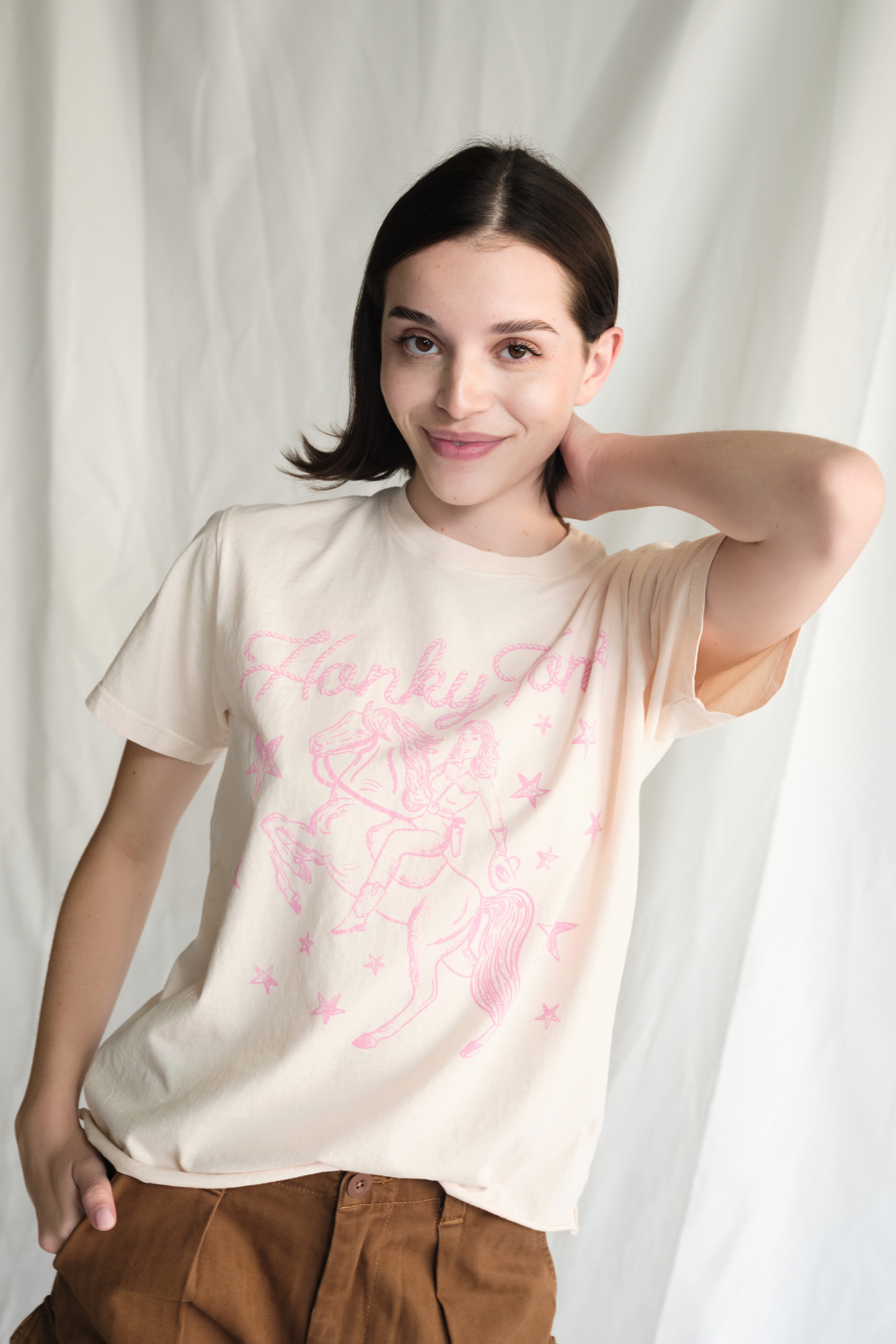 Woman wearing a cream t-shirt with pink graphic design against a white background