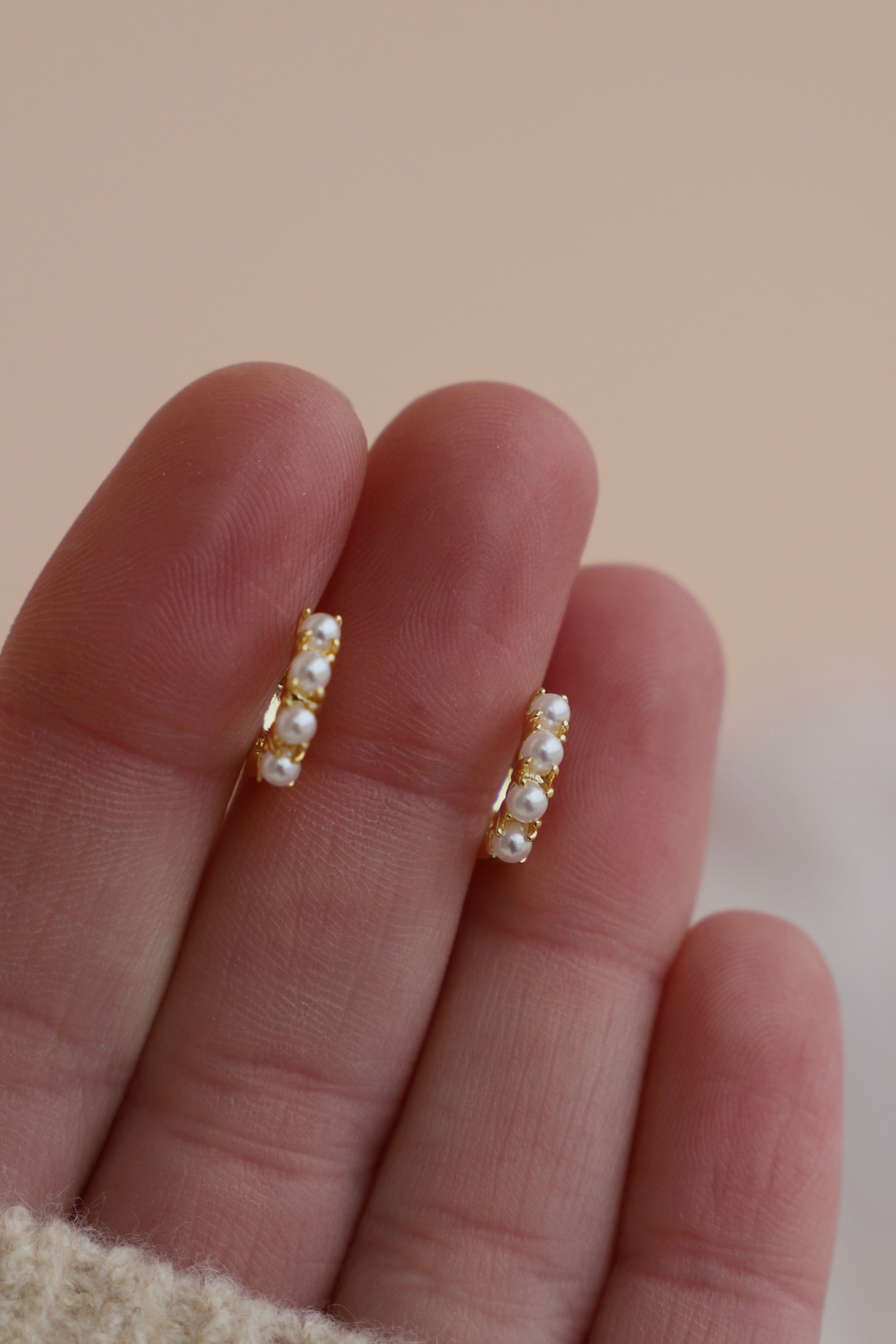 Gold hoop earrings with pearls on a hand against a beige background