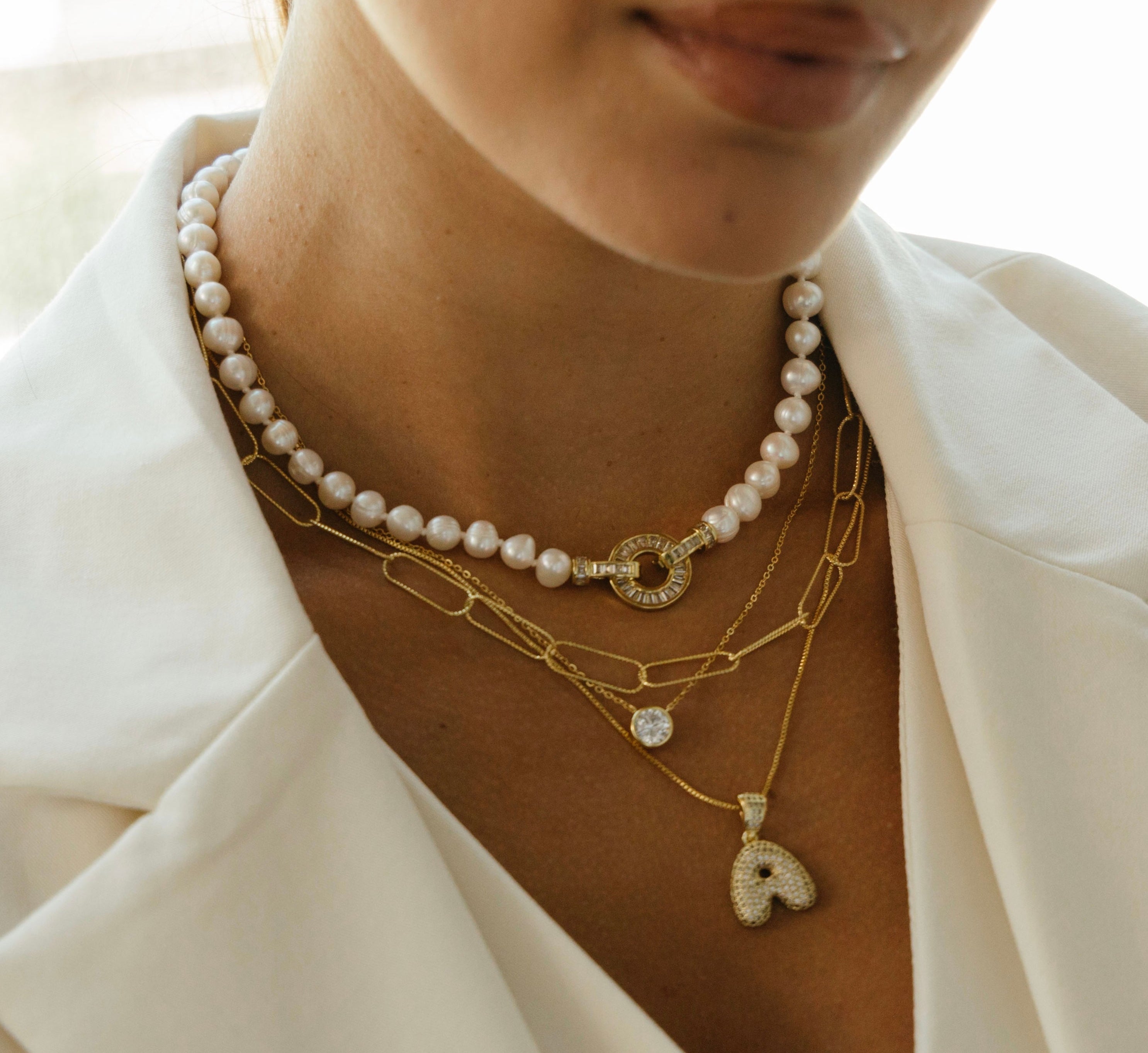 Close-up of a person wearing multiple necklaces with a focus on gold and pearl jewelry.