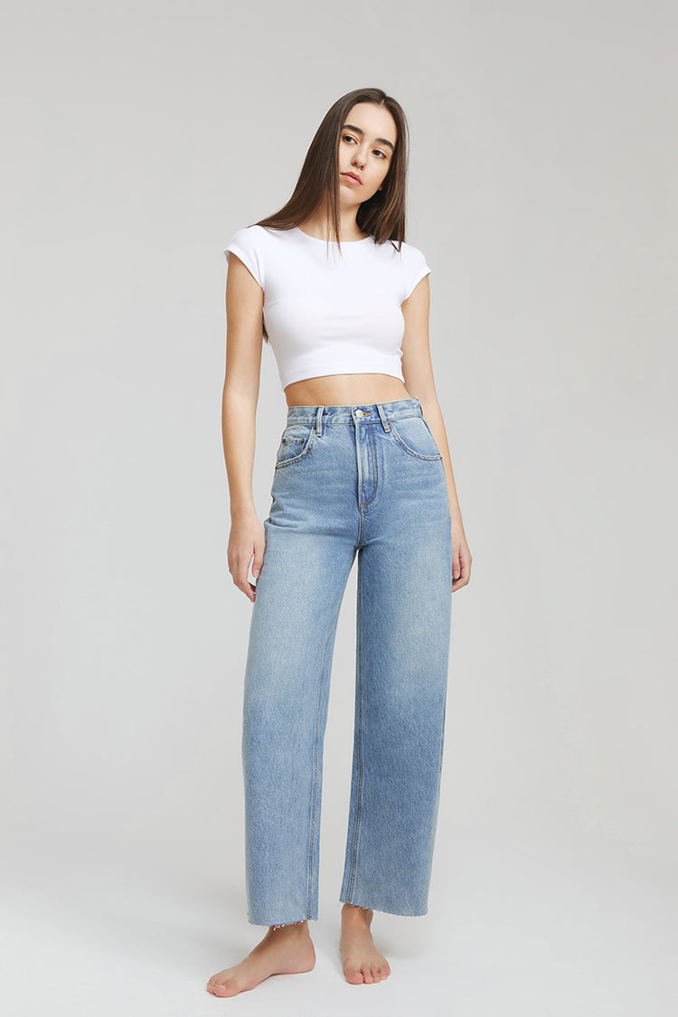 Woman wearing a white crop top and blue jeans on a plain background