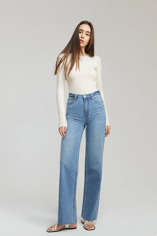 Woman wearing a white top and blue jeans on a plain background