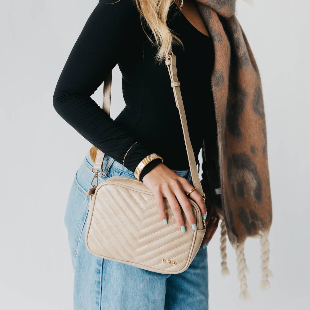 Person holding a beige quilted handbag with a plain background