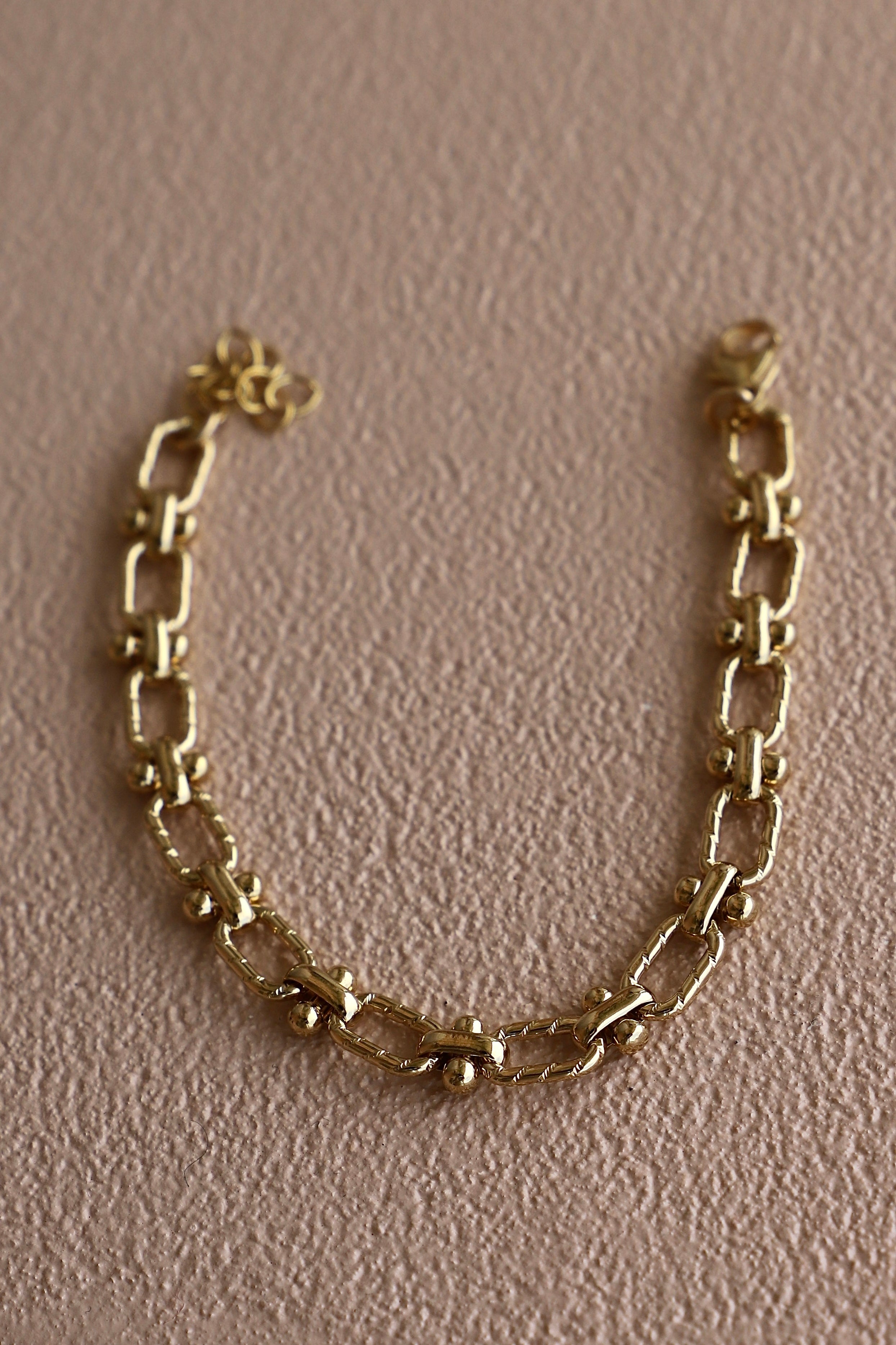 Gold chain bracelet on a pink background
