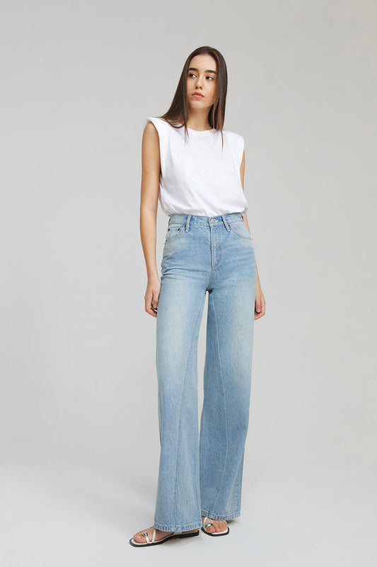 Woman wearing a white sleeveless top and light blue jeans on a gray background