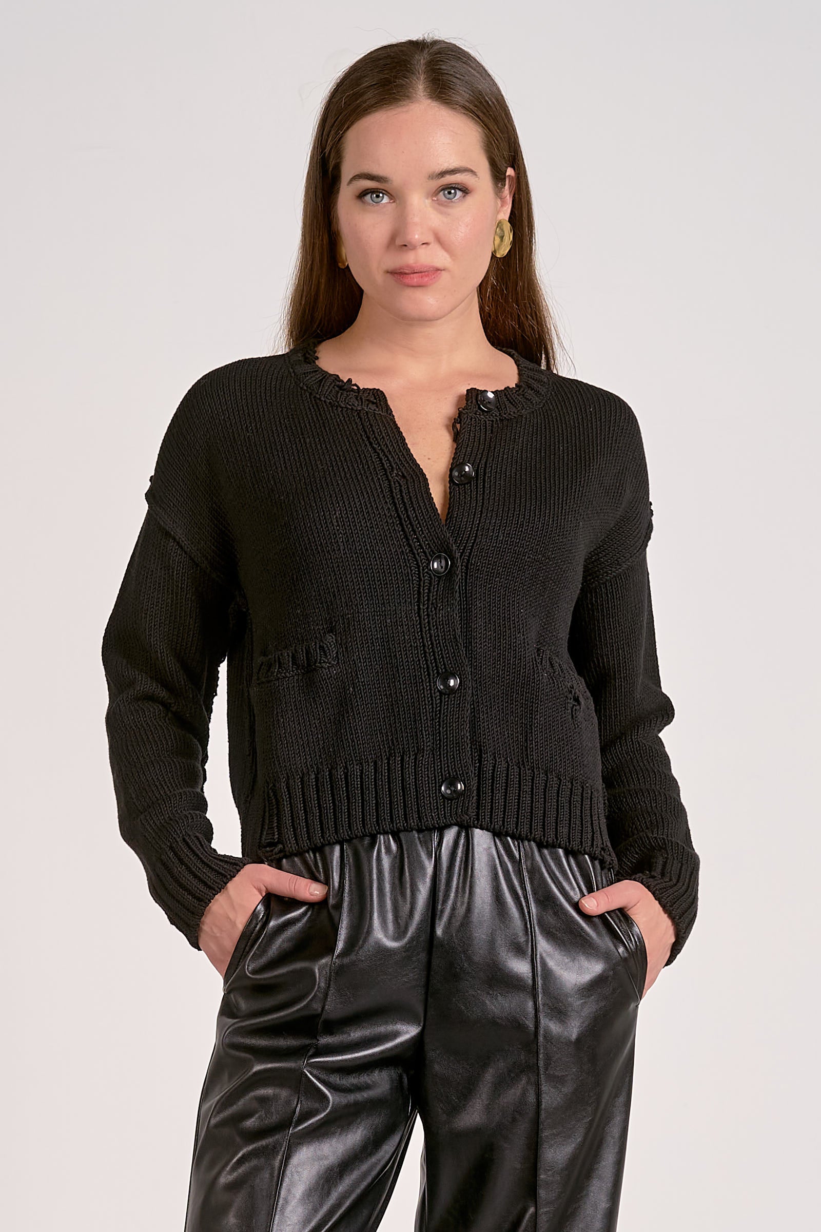 Woman wearing a black cardigan and shiny black pants on a white background