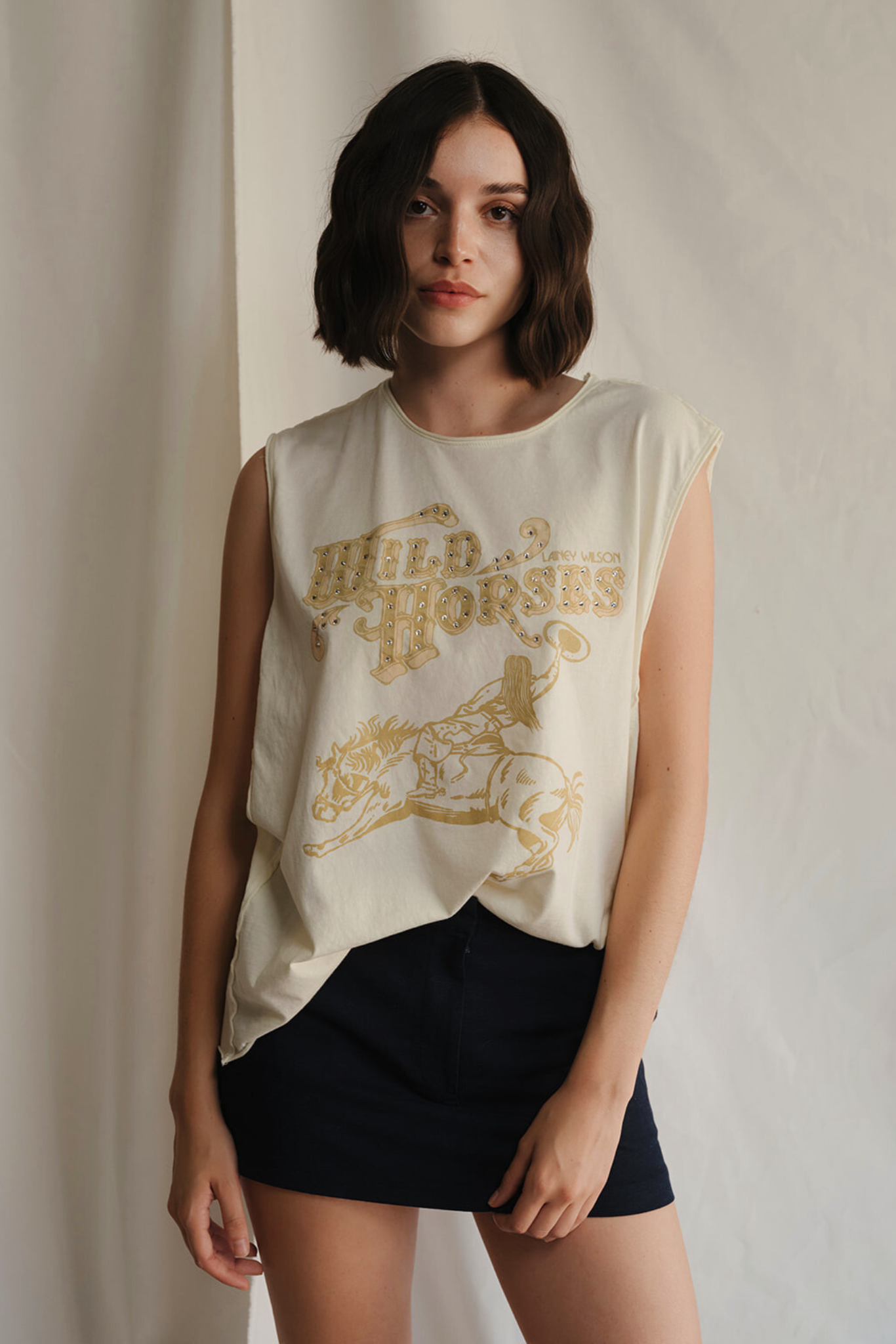 Woman wearing a sleeveless shirt with 'Wild Horses' graphic design against a plain background