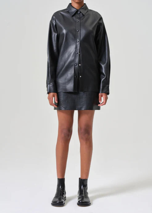 A model wearing the Agolde Agda Mini Recycled Leather Skirt in 'Detox.' The black mini skirt has a sleek, flattering silhouette and a matte finish.
