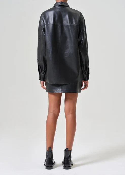 Back view of a model wearing the Agolde Agda Mini Recycled Leather Skirt in 'Detox.' The black mini skirt has a sleek, flattering silhouette and a matte finish.