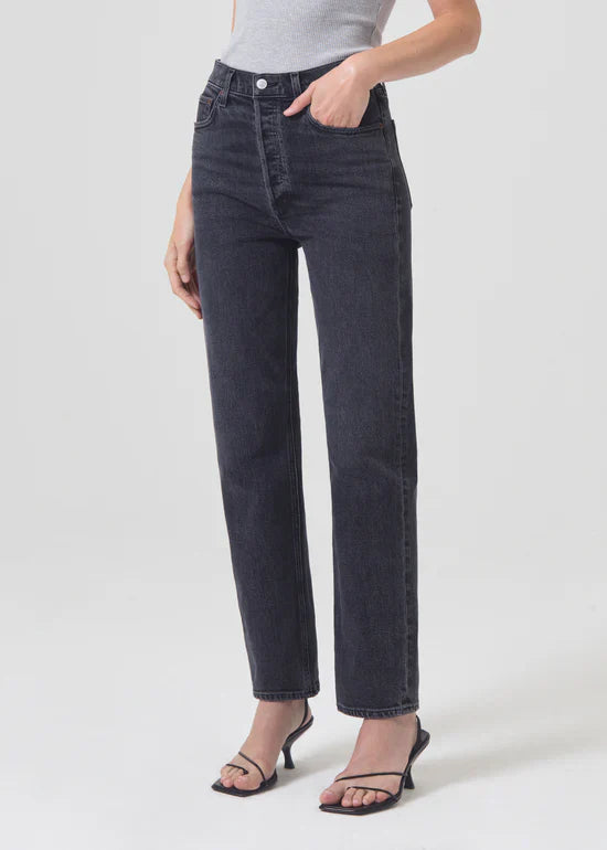 Close-up of the Agolde Stovepipe jeans in "Metal," showing the washed-down black denim texture and zip fly closure.