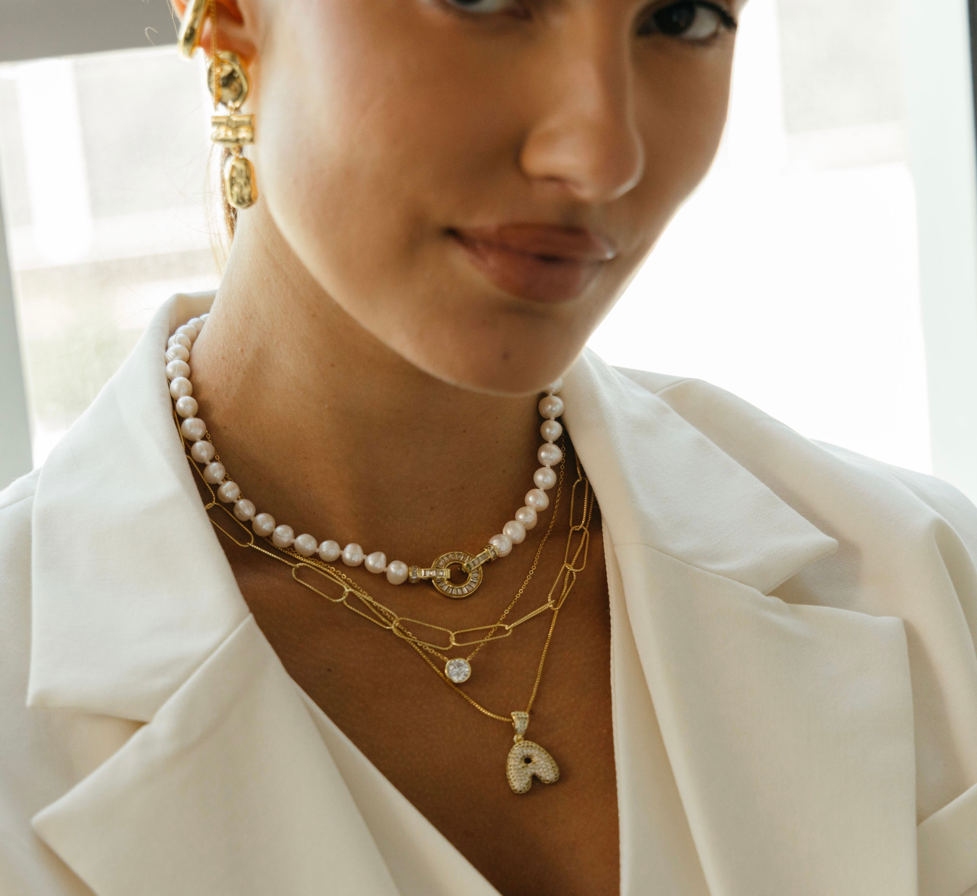 Close-up of a person wearing gold and pearl necklaces with a blurred background