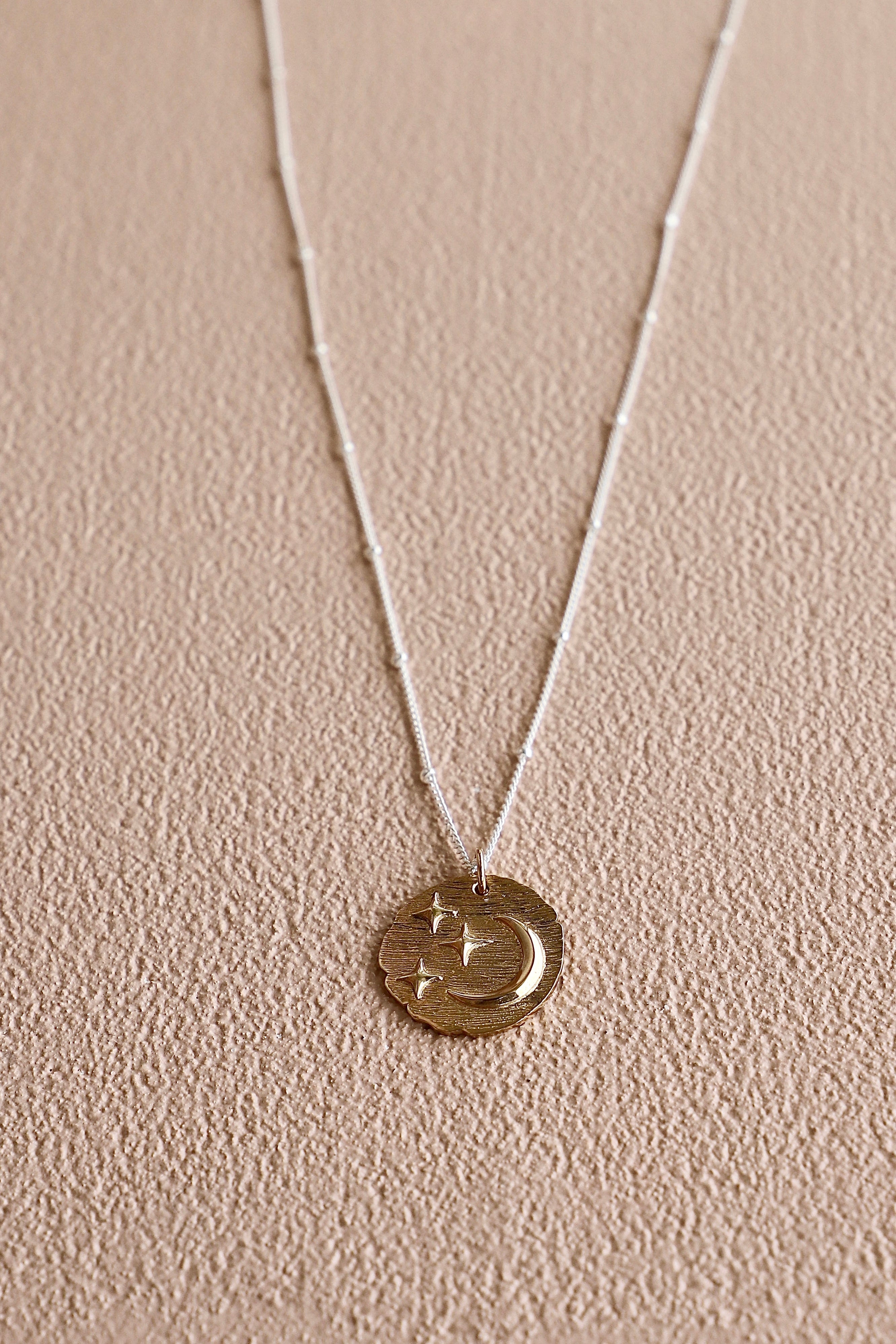 Gold necklace with a round pendant on a beige background