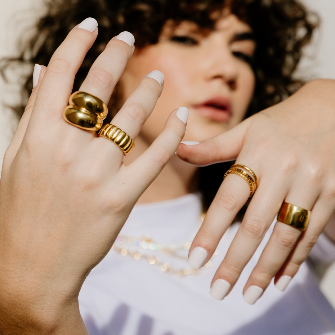 Woman wearing multiple gold rings on her fingers with a neutral background